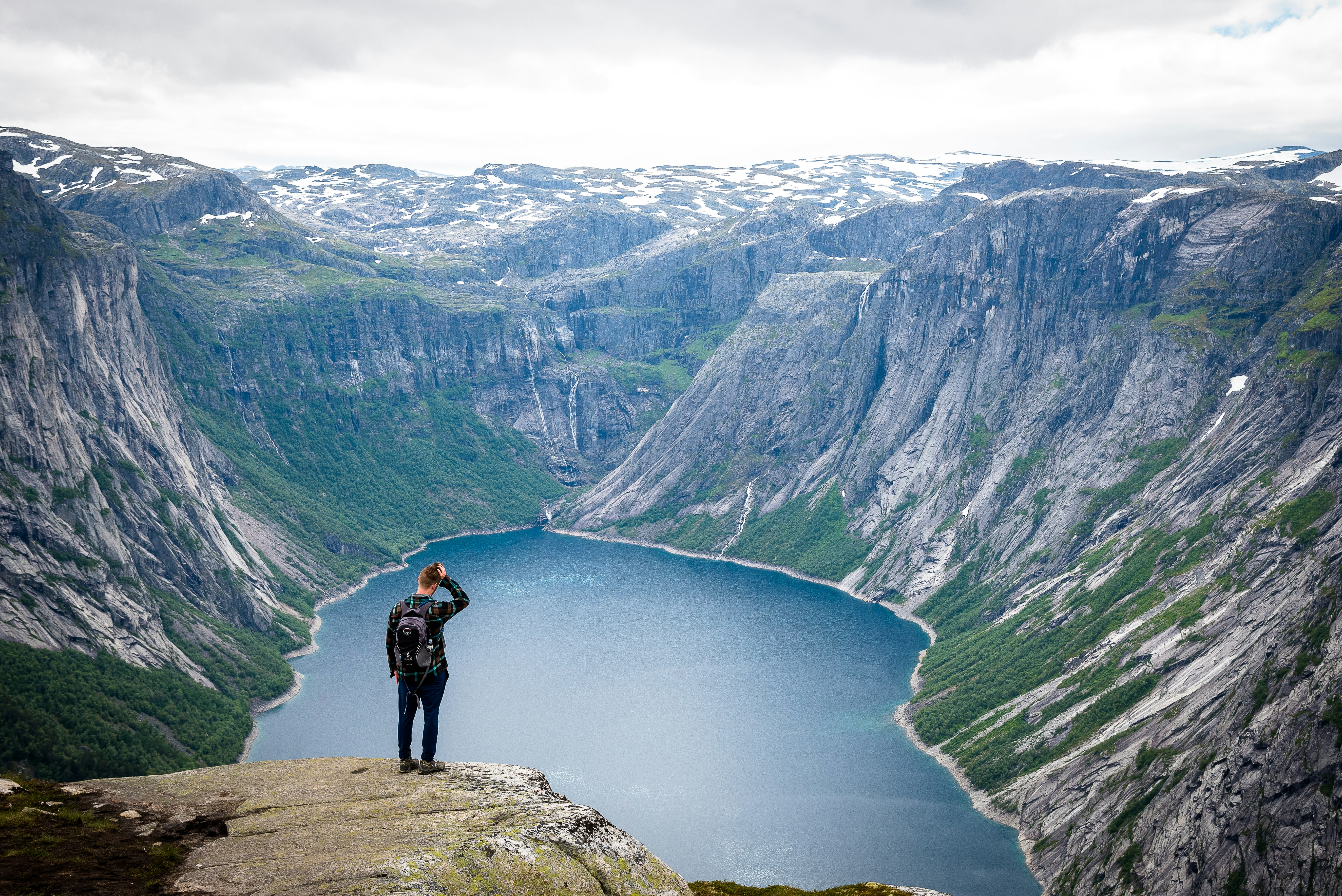 man in black jacket with black backpack standing on top of cliff above a lake at daytime